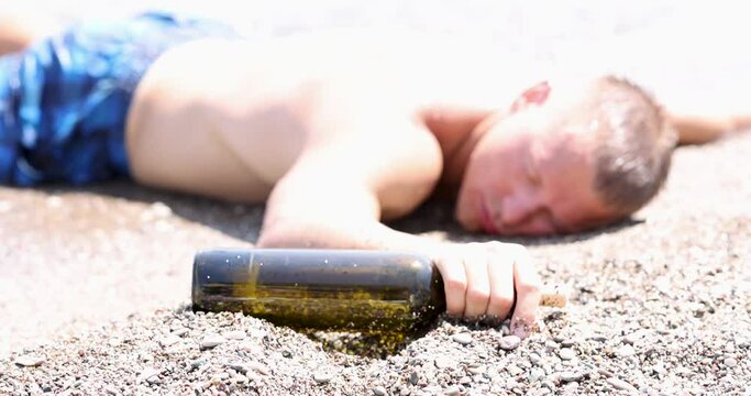 Drunk young man with bottle of wine in his hand lying on seashore 4k movie