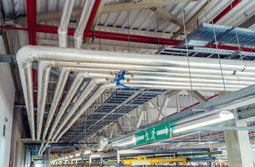 Metal pipes mounted under the ceiling are covered with thermal insulation at a modern production plant