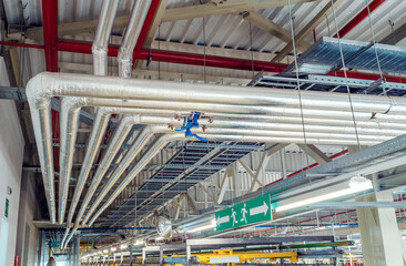 Metal pipes mounted under the ceiling are covered with thermal insulation at a modern production...