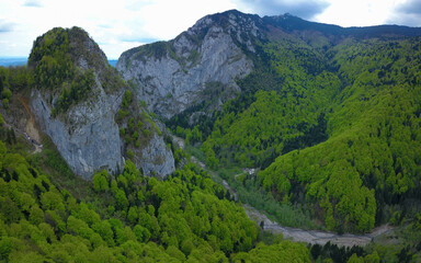 Naklejka premium Aerial drone view above Cheia Valley and Gorges. High steep cliffs are guarding the canyon's entrance. A tunnel dig through the mountain allowed the presence of a gravel road.