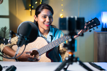 young girl influencer playing guitar during podcast or live video streaming for audience from...