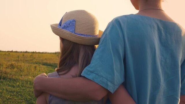 Mother and daughter stand in the meadow of the field in an embrace, the girl has a beautiful greaseproof hat. Relationships in the family, love of mother and daughter in an incomplete family.