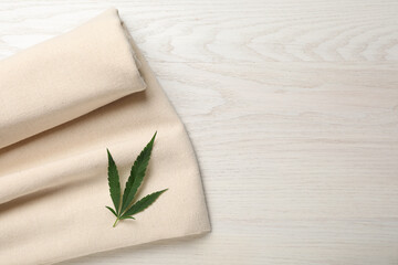 Hemp cloth with green leaf on white wooden table, top view. Space for text