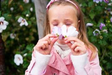 A cute, blond six-year-old girl smells the flowers and enjoying the fragrance with her eyes closed.