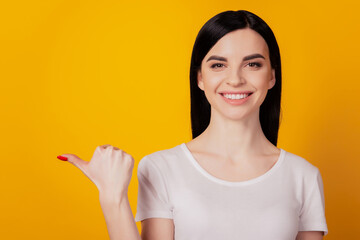 Portrait of cheerful young girl point thumb empty space advertise choose isolated over yellow color background