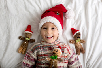 Cute toddler child, holding knitted toy, sitting in bed, playing with pet dog