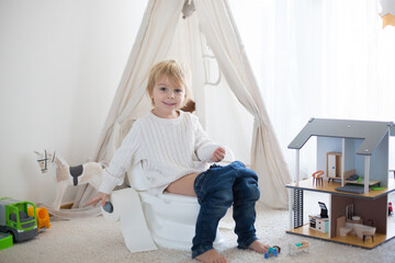 Cute toddler child, boy, sitting on a baby toilet potty, playing