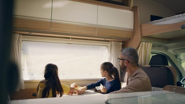 Small girls playing cards with father indoors in caravan, family holiday trip.