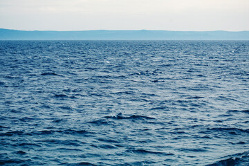 Naklejka na ściany i meble Serene nautical landscape with blue sea water waves, mountains on horizon and light sky