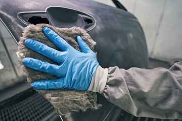 Person in rubber glove wiping car with rag