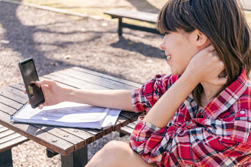 Medium shot of a beautiful woman sitting on a bench in the plaza, checking messages on her cell phone, smiling. Telecommunications, technology, internet concept.