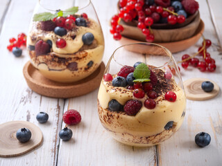 Homemade tiramisu in transparent cups with red currant, blueberry, raspberry on a white wooden table. Horizontal.