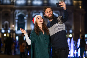 Cute cheerful couple with sparklers rejoices on New Year's Eve taking a selfie on a mobile phone, the couple is happy