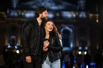 Young couple posing on the street against the backdrop of the night city. Pretty pretty woman and her handsome stylish boyfriend are hugging