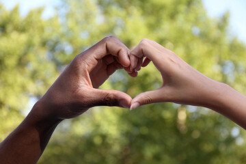 Woman and African American man making heart with hands outdoors, closeup
