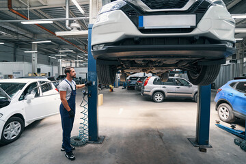 Auto mechanic looking at a car on direct lift hoist