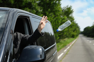 Driver throwing away plastic bottle from car window. Garbage on road