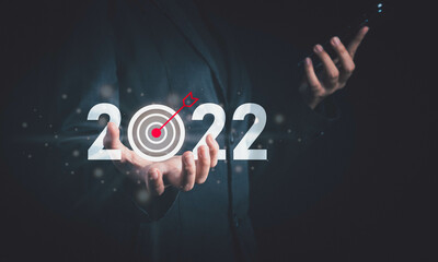 Target and goal of 2022. New year start success  plan and vision. Hand hold smartphone and target arrow 2022 icon in dark tone.