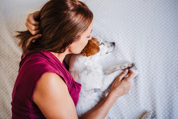 top view of young caucasian woman at home resting on bed with cute jack russell dog. Woman kissing dog. Pets, love and relax