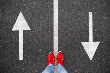 Red sneakers on the asphalt road with drawn arrows pointing to two directions. Making decisions and...