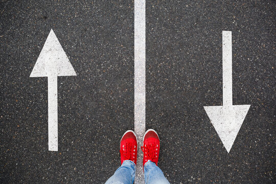 Red sneakers on the asphalt road with drawn arrows pointing to two directions. Making decisions and making choices