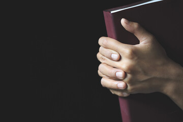 Hands folded in prayer on a Holy Bible  in church concept for faith, spirtuality and religion,...