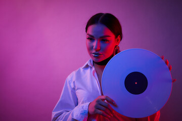 Disco woman portrait holding a retro vinyl with 80s music on neon light background.