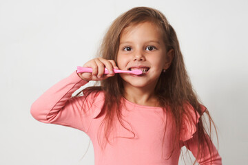 Little child girl brushing her teeth on white background.