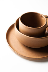 Vertical of overlapping brown pottery coffee cup, bowl and plate, isolated on white