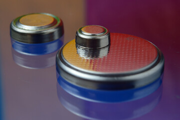 small button batteries of different sizes, highlighted in red and orange, lie against a blue background. close-up.