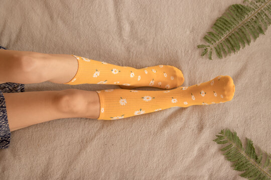 Female legs with long yellow socks with daisies on top of a bed