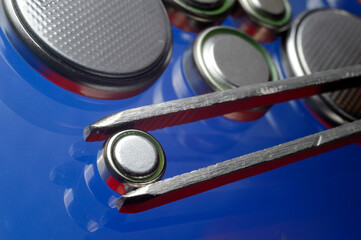 a small battery clamped with tweezers against the background of other small batteries. close-up.