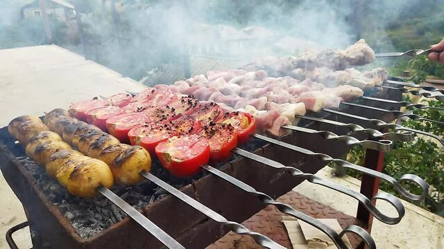 Shashlik on the fire. Barbecue, BBQ. The cook prepares barbecue in the village. Pork meat on fire. Red tomatoes, yellow shorties and pork meat on the fire. Flight dish from the cook
