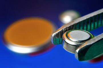 a small battery clamped with tweezers against the background of other small batteries. close-up.