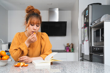 Caucasian woman eating a tangerine while reading a book on a table