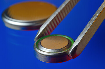 a small battery clamped with tweezers against the background of other small batteries. close-up.