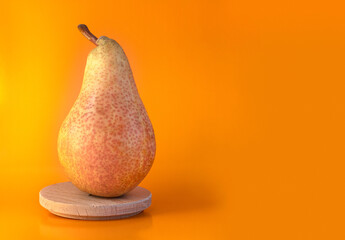 Pear standing in a front view on a wooden plate. Yellow fruit in the orange paper background