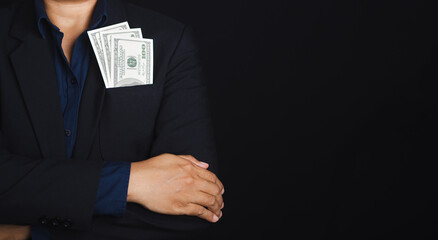 Businessman wearing a suit with US dollars in a suit pocket and arms crossed while standing in a studio with a black background with space for text. Business and finance concept
