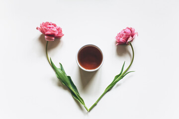A cup of coffee or tea on a white background with pink tulips. Creative concept, flat lay, top view