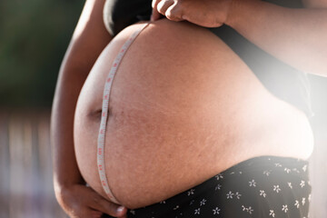 pregnant woman measuring tape around protuberant abdomen.