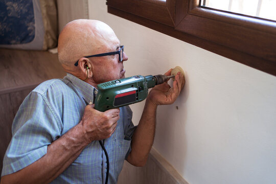 Focused senior man screwing detail to wall at home