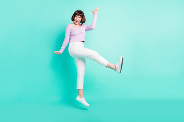 Fototapeta na wymiar Full length photo of cute adorable young lady wear purple pullover walking jumping high smiling isolated teal color background