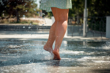 slender beautiful female legs in splashes of water. outdoor city fountain.