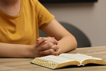 Religious woman praying over Bible at wooden table indoors, closeup
