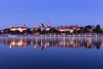 Illuminated Warsaw Old Town landscape with the Royal Castle, Cathedral and medieval buildings, night view with reflections in calm Vistula river, Poland.