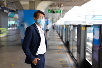 Asian business man wearing face masks while commuting by public transport station during COVID-19 pandemic.