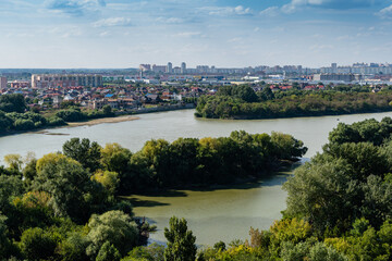 Fototapeta na wymiar New microdistrict with high-rise residential buildings, shopping centers and new buildings on banks of Kuban River. Trees are overgrown in middle of the river. Krasnodar, Russia - September 05, 2021