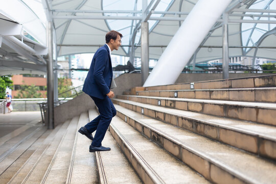 Asian businessman wearing suit jacket running fast upstairs go to work in morning outdoor.