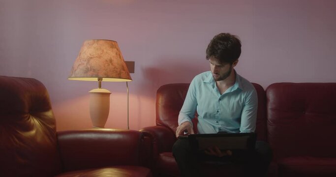 Ragazzo con camicia azzurra usa il computer portatile sulle gambe seduto sul divano