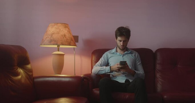 Giovane ragazzo usa lo smartphone seduto sul divano di casa la sera